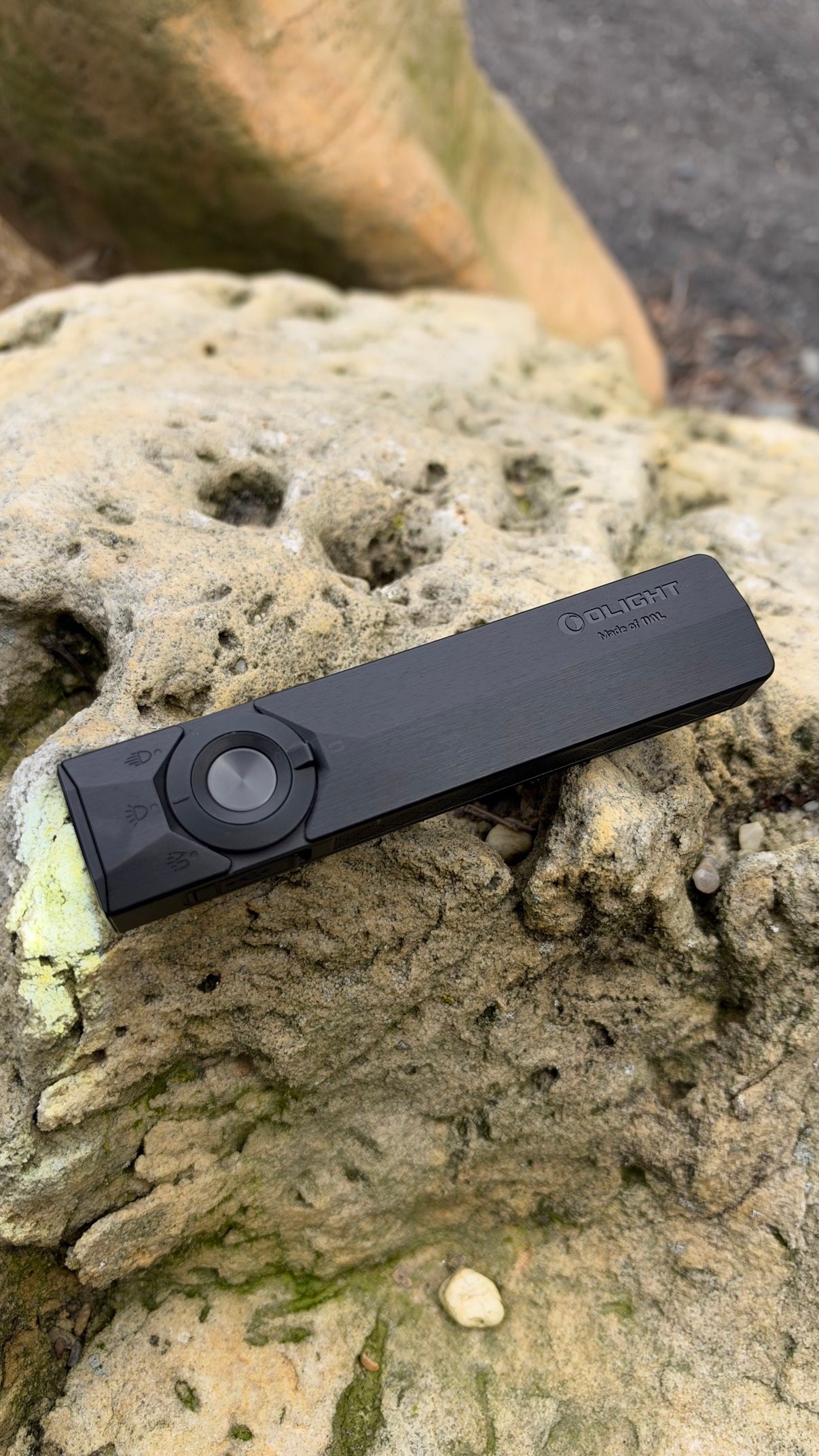 Black OLIGHT ArkPro Ultra flashlight on a rock