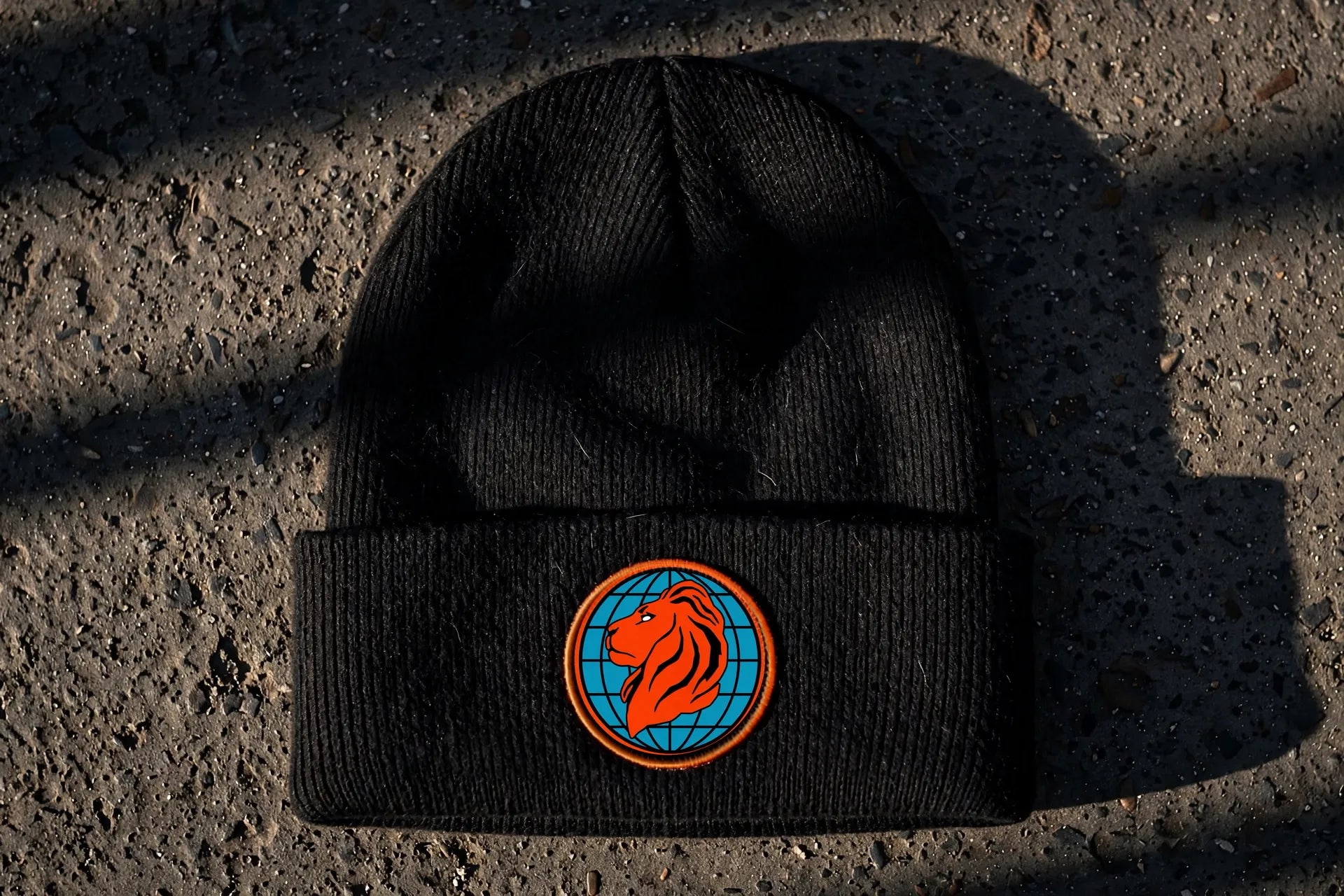 Black rib-knit beanie on concrete with the blue and orange WDGTOOLS lion globe logo