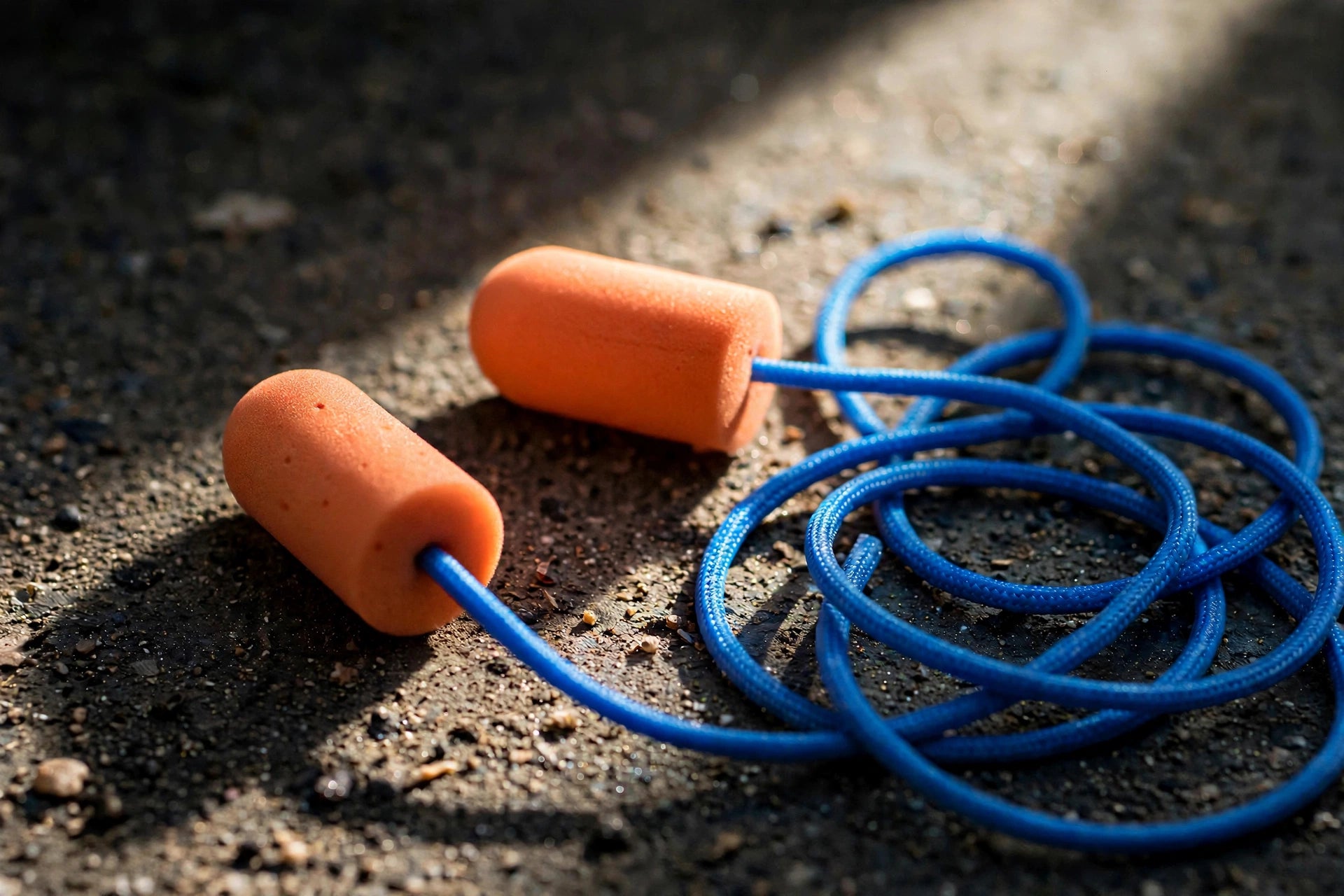 Orange foam ear plugs with a blue cord on concrete